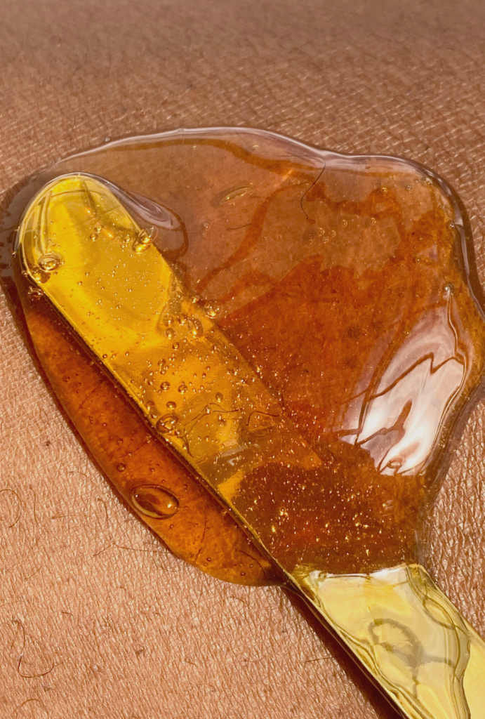 A close-up photo of soft sugar wax being applied to the skin in the opposite direction of hair growth using the OLI golden applicator